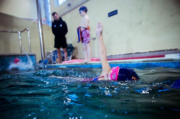 Group swimming and a child swims front crawl in group lessons at Blue Wave